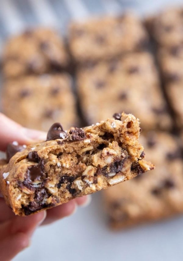 Hang holding an almond butter oatmeal cookie bar with more cookie bars in the background.