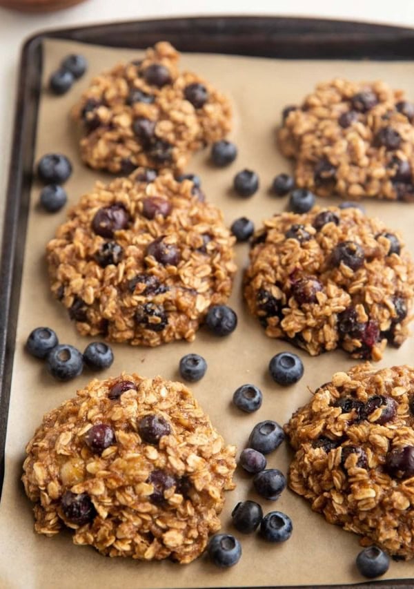 Blueberry Oatmeal Cookies on a baking sheet with fresh blueberries scattered around.