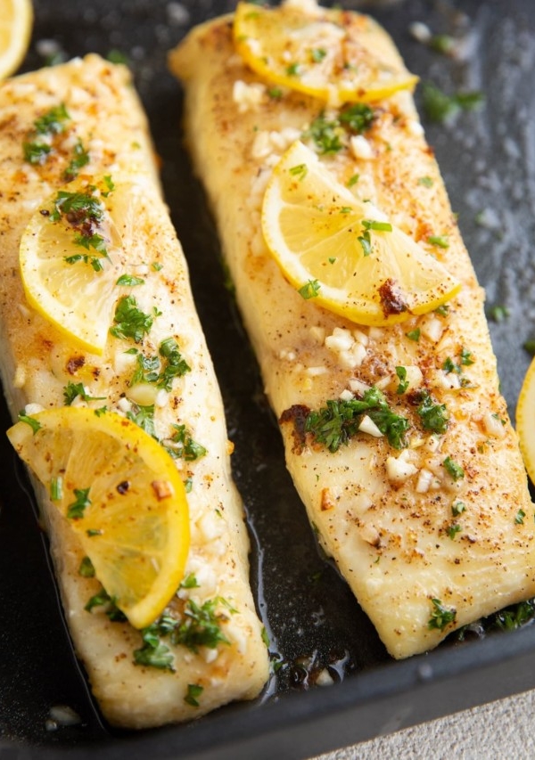 Two cooked halibut filets with butter, fresh garlic, and lemon on top