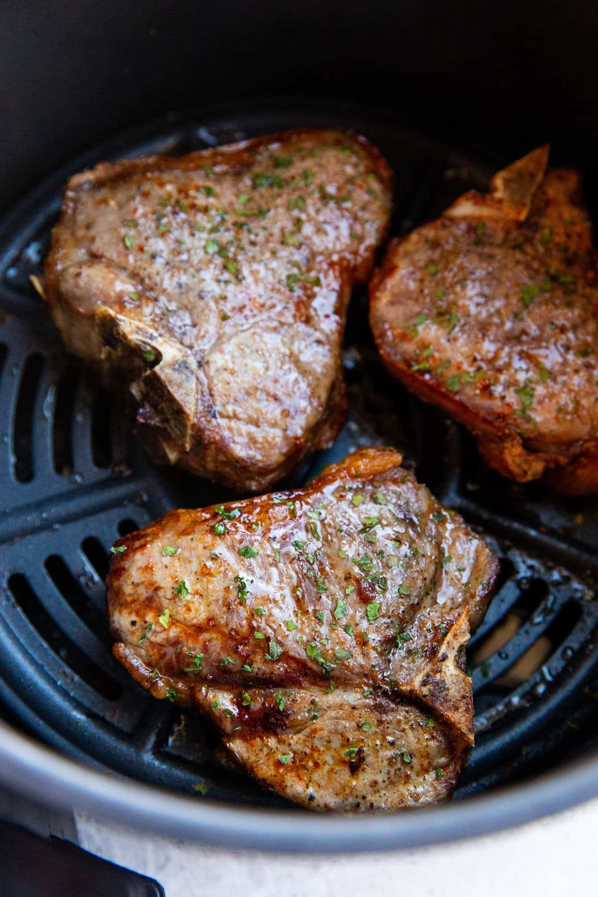 Basket of an air fryer with pork chops inside.