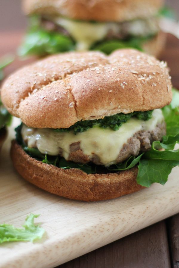 Lamb Burgers with Mint Pesto and Jack Cheese on a cutting board with more burgers in the background, ready to eat.