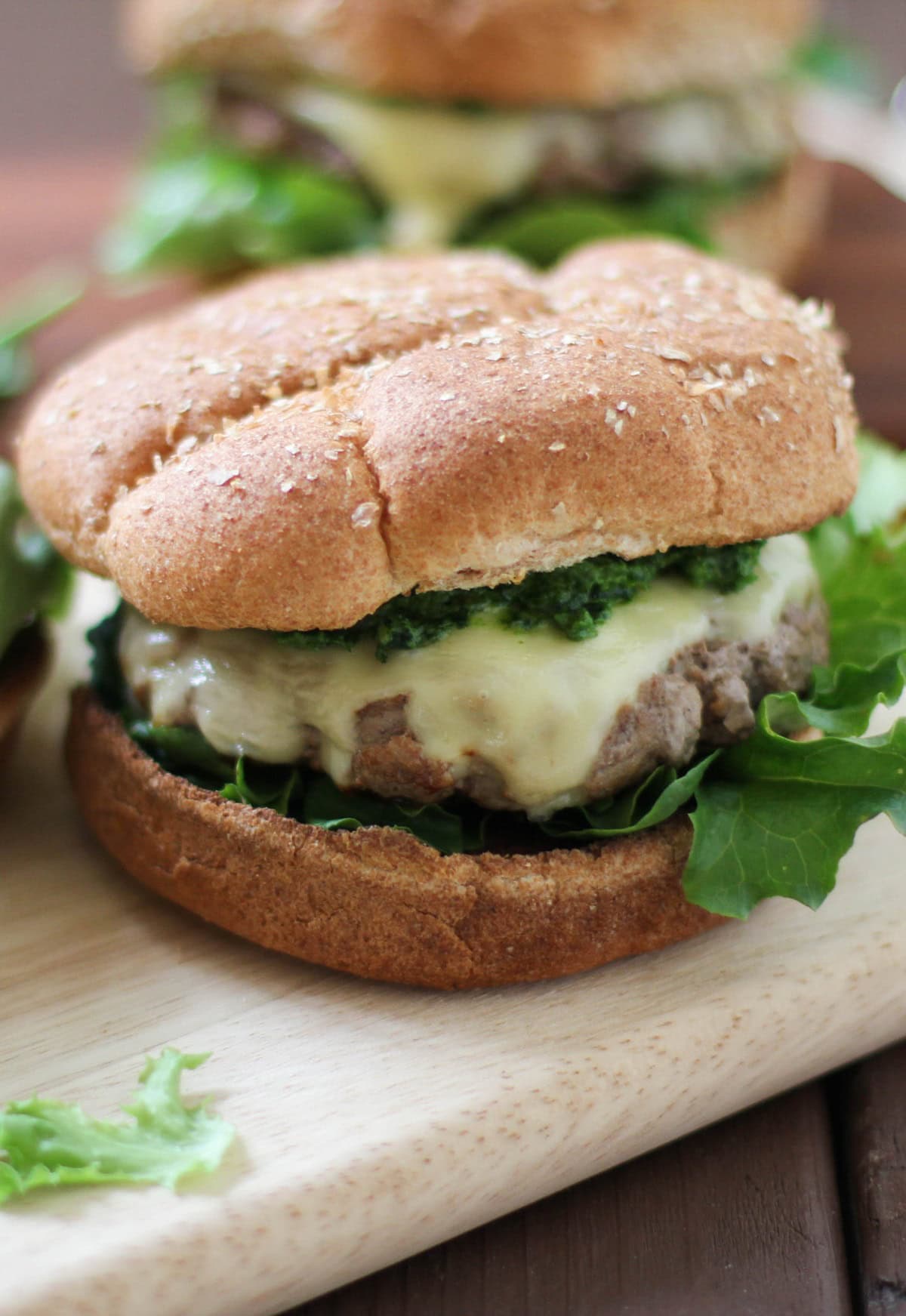 Lamb Burgers with Mint Pesto and Jack Cheese on a cutting board with more burgers in the background, ready to eat.