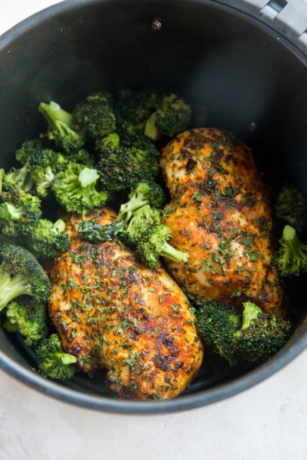 Air fryer with chicken and broccoli inside.