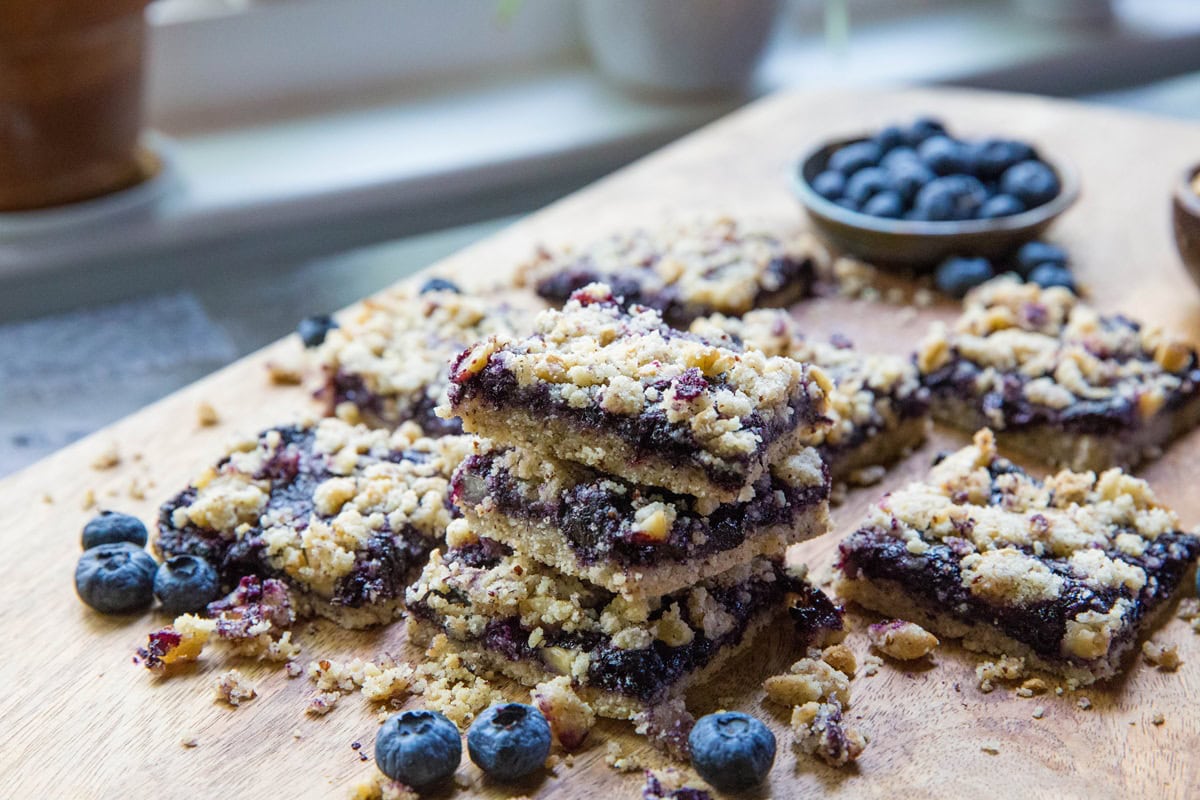 Stack of blueberry crumb bars on a cutting board with fresh blueberries in the background.