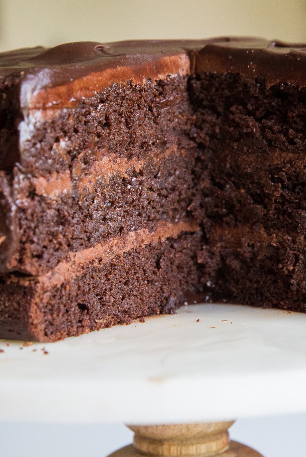 Three layer chocolate cake on a cake stand with a large chunk taken out so you can see the layers of frosting between the layers of cake