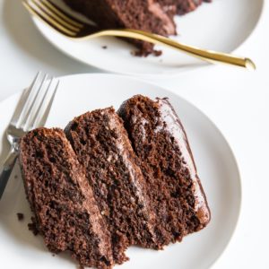 Two slices of three layer chocolate cake with golden forks, ready to serve.