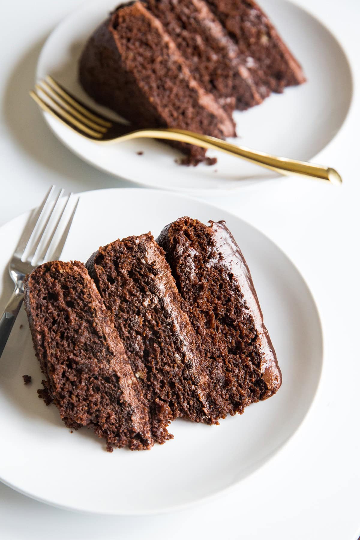 Two slices of three layer chocolate cake with golden forks, ready to serve.