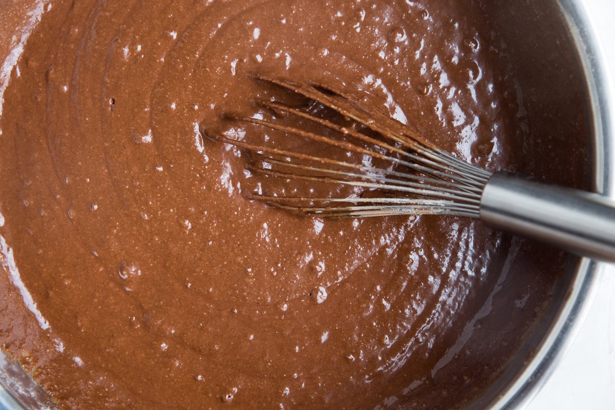 Smooth chocolate cake batter in a stainless steel bowl with a whisk, ready to be used.