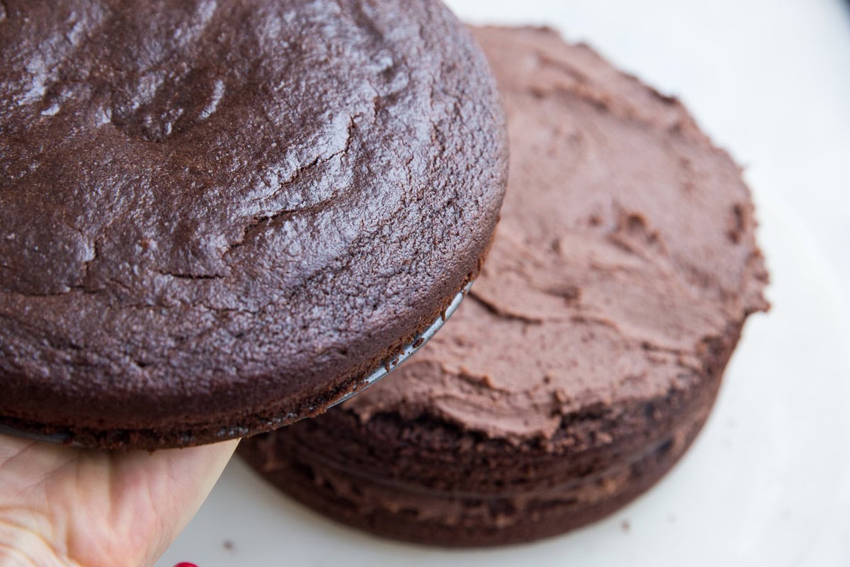 Hand holding a cake to layer on top of two other layers, creating the final layer.