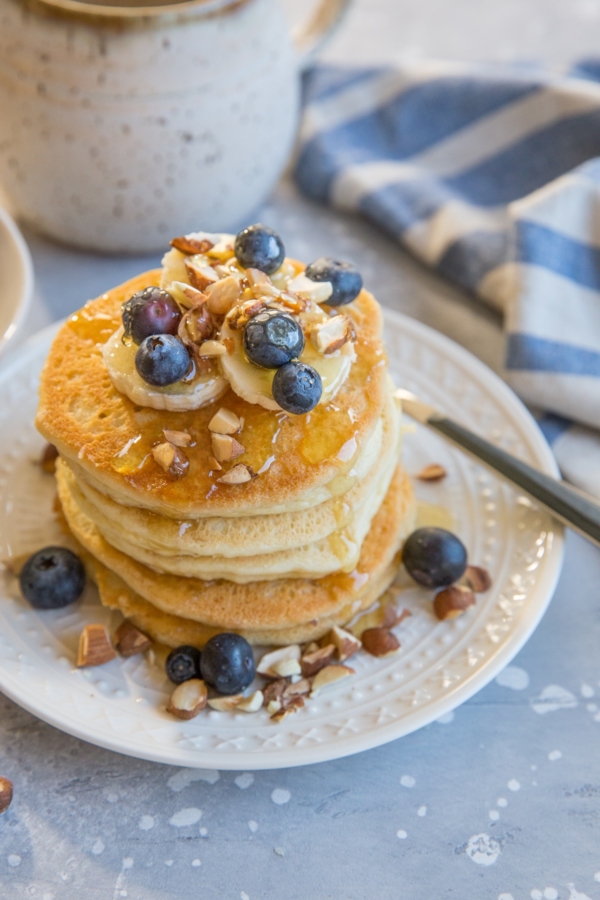 Stack of almond flour pancakes with sliced bananas, fresh blueberries and honey drizzle