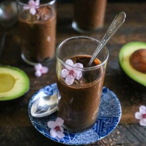 Three dessert glasses with chocolate mousse inside with chocolate shavings all around.