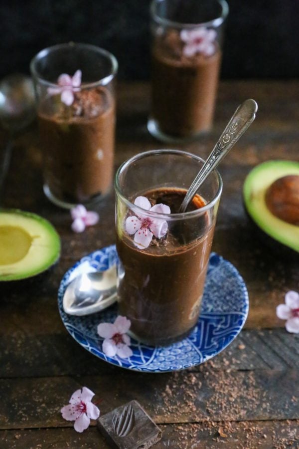 Three dessert glasses with chocolate mousse inside with chocolate shavings all around.