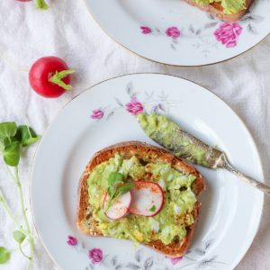 Two plates with two avocado egg salad toasts on top. Fresh microgreens and radishes to the side.