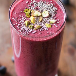 large glass of beet smoothie with chia seeds and chopped pistachios on top.