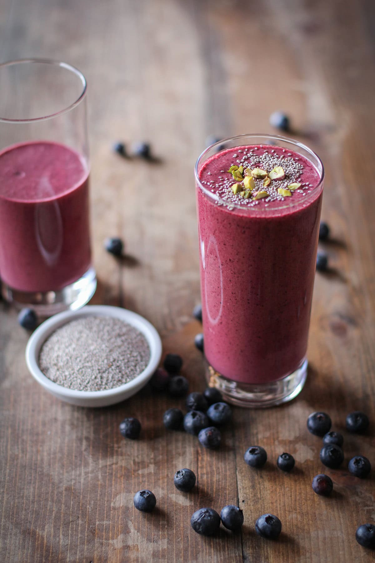 Two glasses of beet smoothie with fresh blueberries all around. Ready to drink!