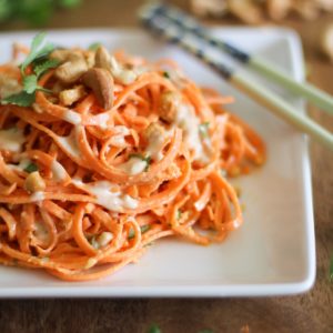 Pile of carrot pasta on a white plate with chopsticks to the side, ready to serve.