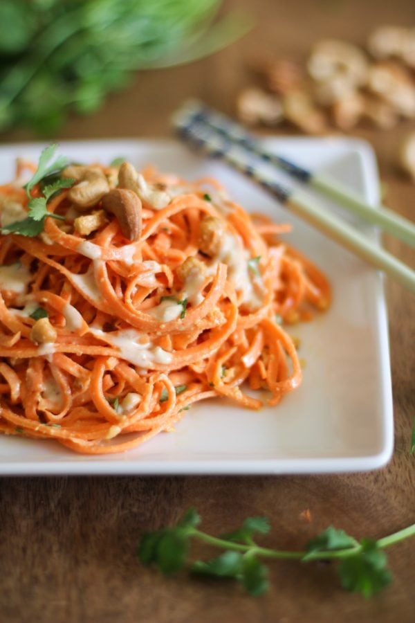 Pile of carrot pasta on a white plate with chopsticks to the side, ready to serve.