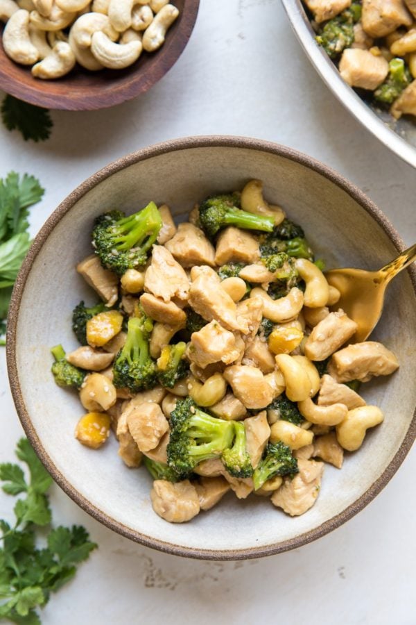 Sesame Ginger Cashew Chicken with broccoli in a bowl with a golden spoon and fresh cilantro to the side, ready to eat.