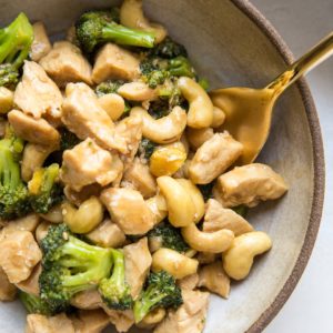 Big bowl of cashew chicken with broccoli, with a golden spoon. Ready to eat.