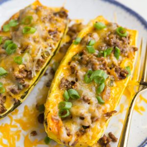 Taco Stuffed Delicata Squash with spiced ground beef, onion, and cheese on a plate with a golden fork, ready to eat.