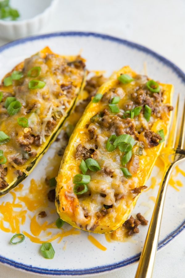 Taco Stuffed Delicata Squash with spiced ground beef, onion, and cheese on a plate with a golden fork, ready to eat.