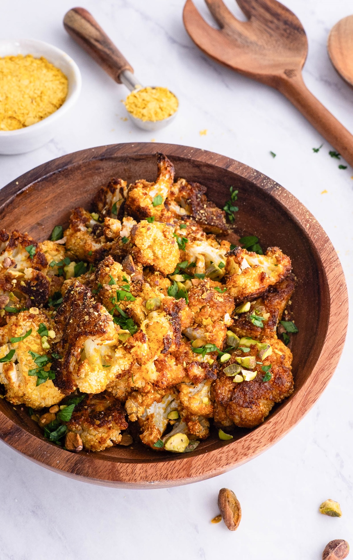 Wooden bowl full of cheesy vegan roasted cauliflower sprinkled with pistachios and ready to serve.