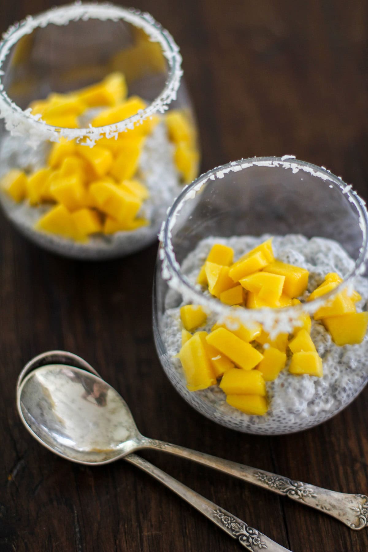 Two glasses filled with chia seed pudding with fresh chopped mango on top.