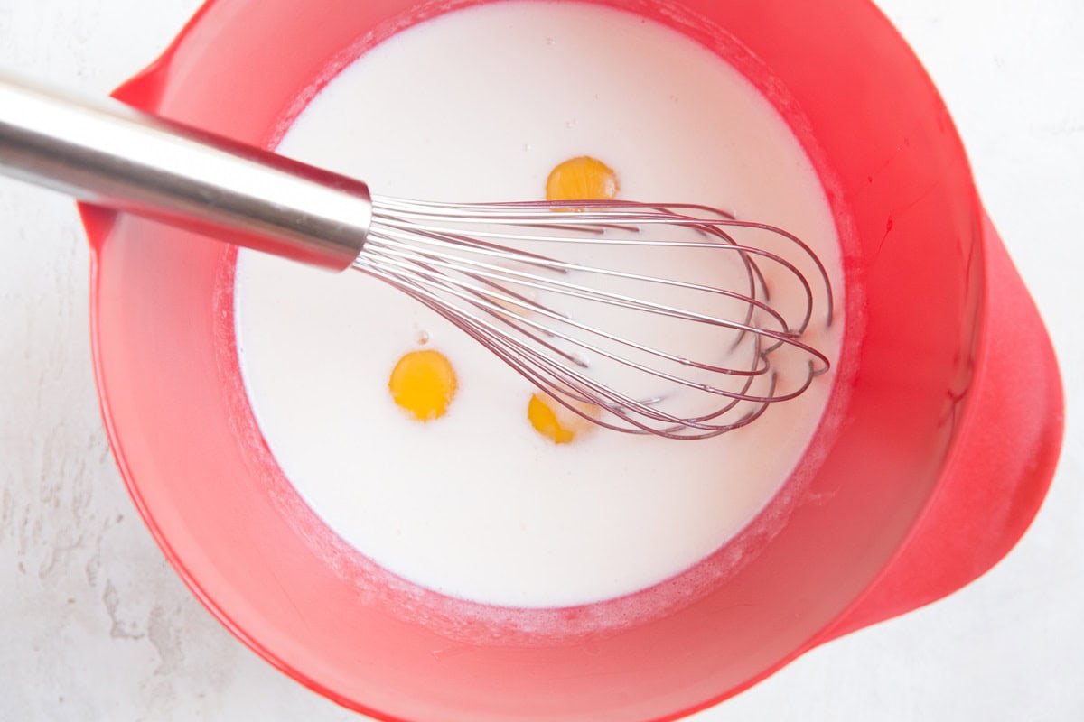 Large red mixing bowl with milk and eggs inside, to be whisked.