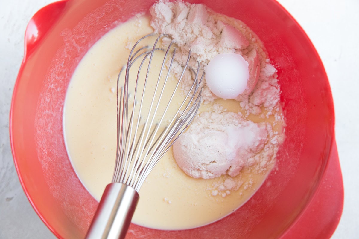 Wet ingredients in a mixing bowl with dry ingredients added on top.