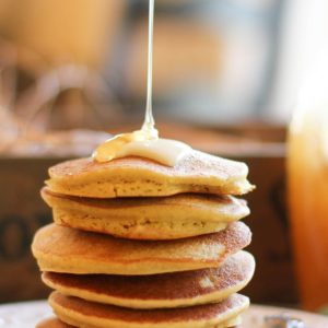 Stack of cornbread pancakes on a plate with honey drizzling on top with a fork to the side.