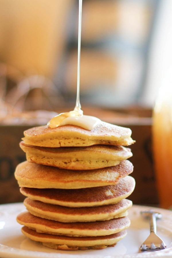 Stack of cornbread pancakes on a plate with honey drizzling on top with a fork to the side.