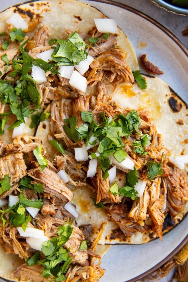 Shredded pork tacos on a plate with cilantro and white onion sprinkled on top.