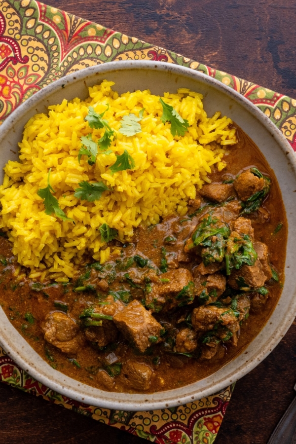 Bowl of lamb curry with saffron rice with a decorative napkin and silver forks.