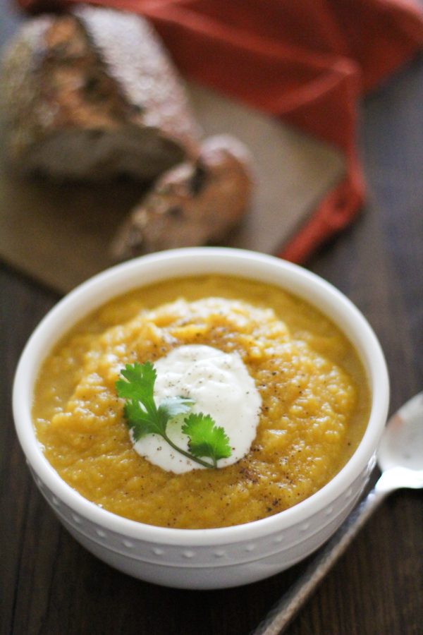 Butternut squash soup in a white bowl with yogurt and cilantro on top and a spoon to the side.