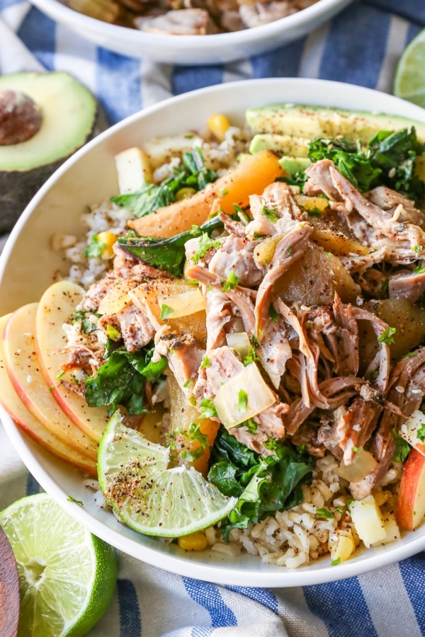 White bowl full of Crock Pot Pulled Pork, apples, brown rice, with Sauteed Kale and Avocado