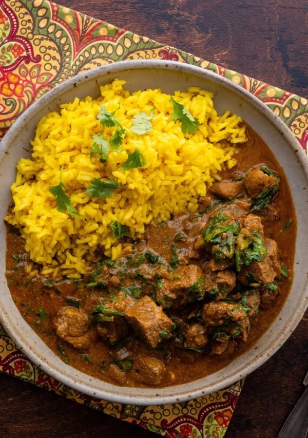 Bowl of lamb curry with saffron rice with a decorative napkin and silver forks.