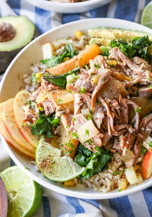 White bowl full of Crock Pot Pulled Pork, apples, brown rice, with Sauteed Kale and Avocado