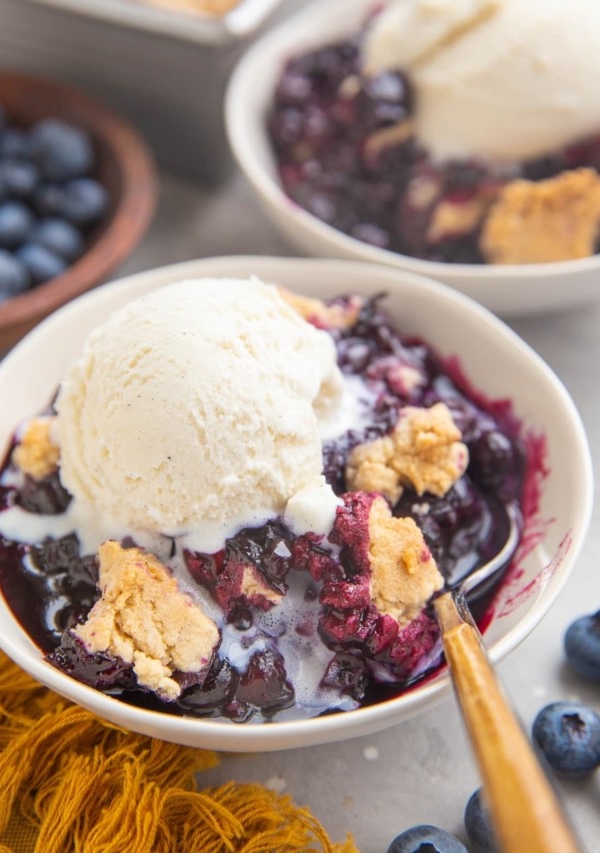 Two bowls of blueberry cobbler with ice cream on top.