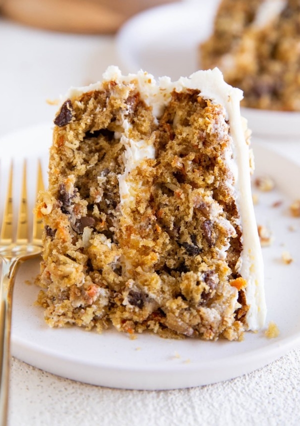 Thick slice of carrot cake on a white plate with a gold fork.