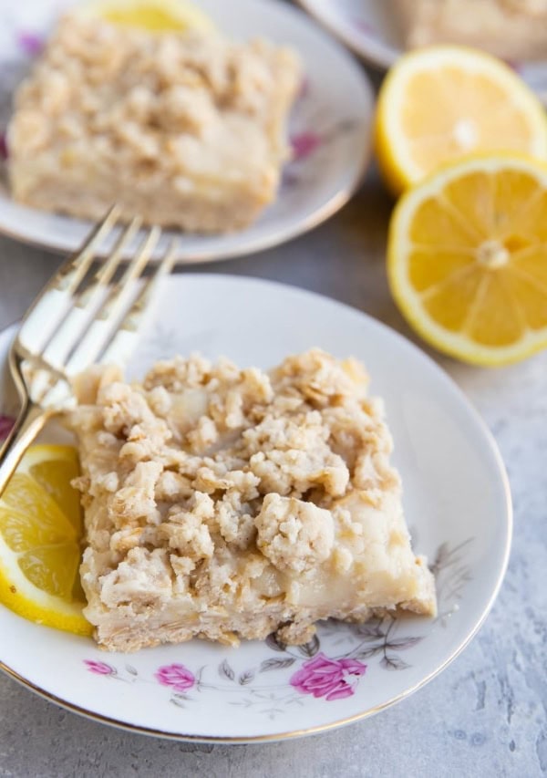 Three decorative plates with roses on them with a lemon crumb bar on top and fork to the side. Fresh lemons in the background.