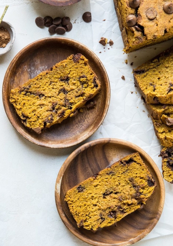 Two wooden plates with slices of pumpkin bread and the rest of the loaf off to the side.