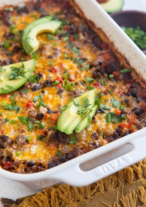 Casserole dish with ground beef casserole inside. Fresh avocado and a bowl of green onions to the side.