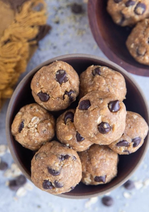 Close up of two bowls with energy balls inside, ready to eat. Chocolate chips and oats sprinkled around the bowls with a golden napkin.