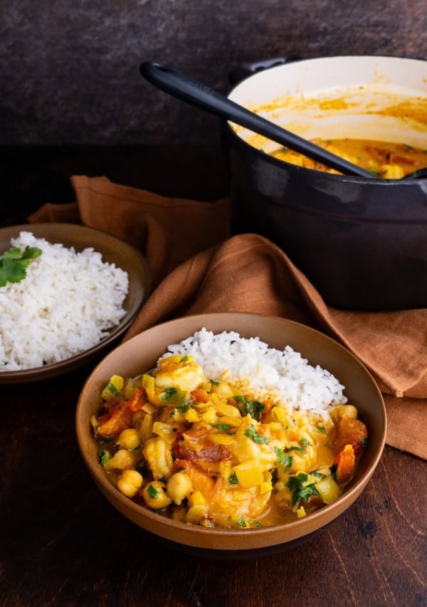 Shrimp curry in a brown ceramic bowl with the pot of the rest of the curry in the background.