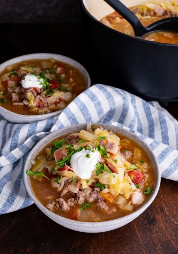 Sausage and cabbage stew in two bowls with a pot of soup in the background