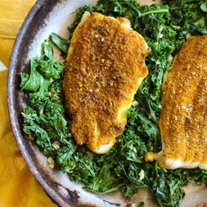 Skillet with two petrale sole filets on top of a bed of kale.