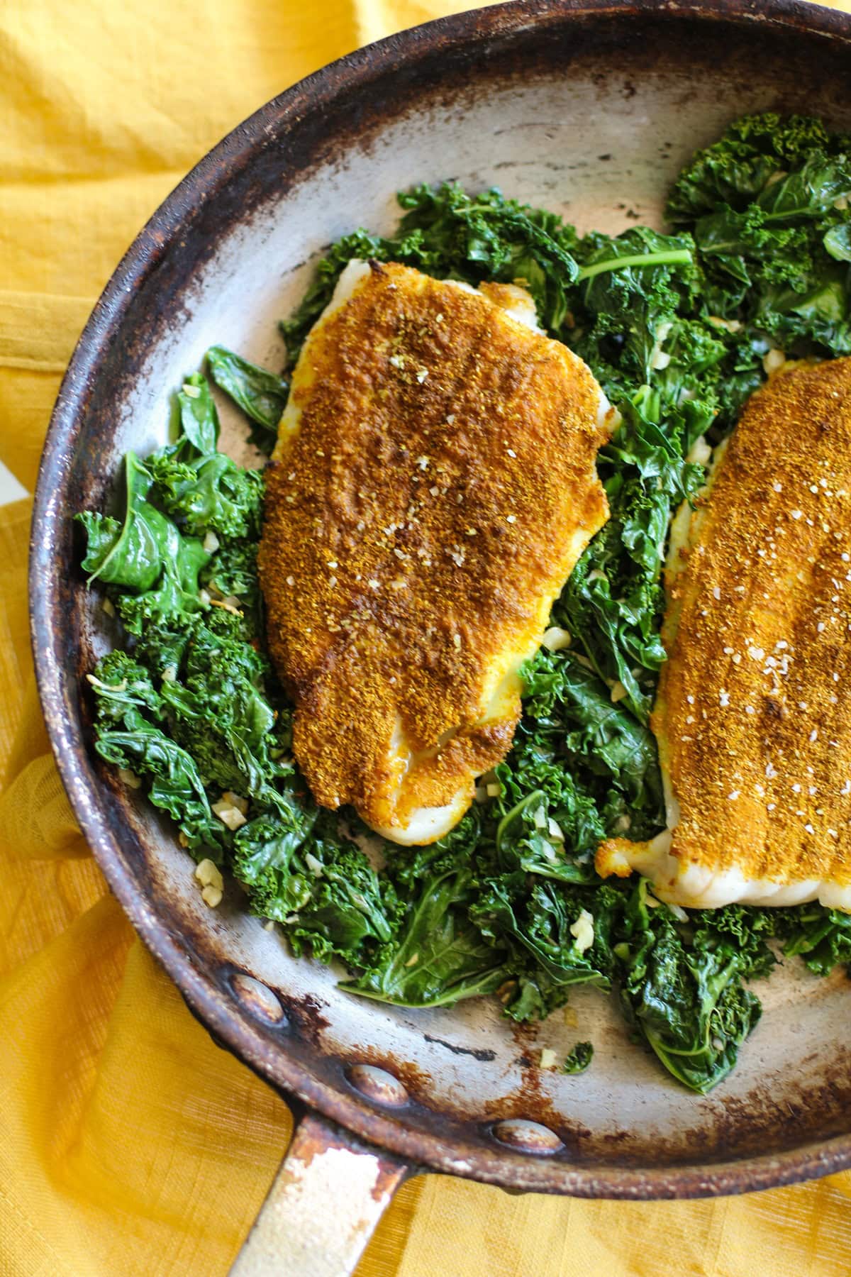 Skillet with two petrale sole filets on top of a bed of kale.