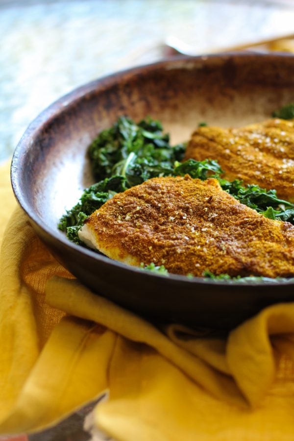 Skillet with two cooked sole filets on top of sauteed kale, ready to serve.