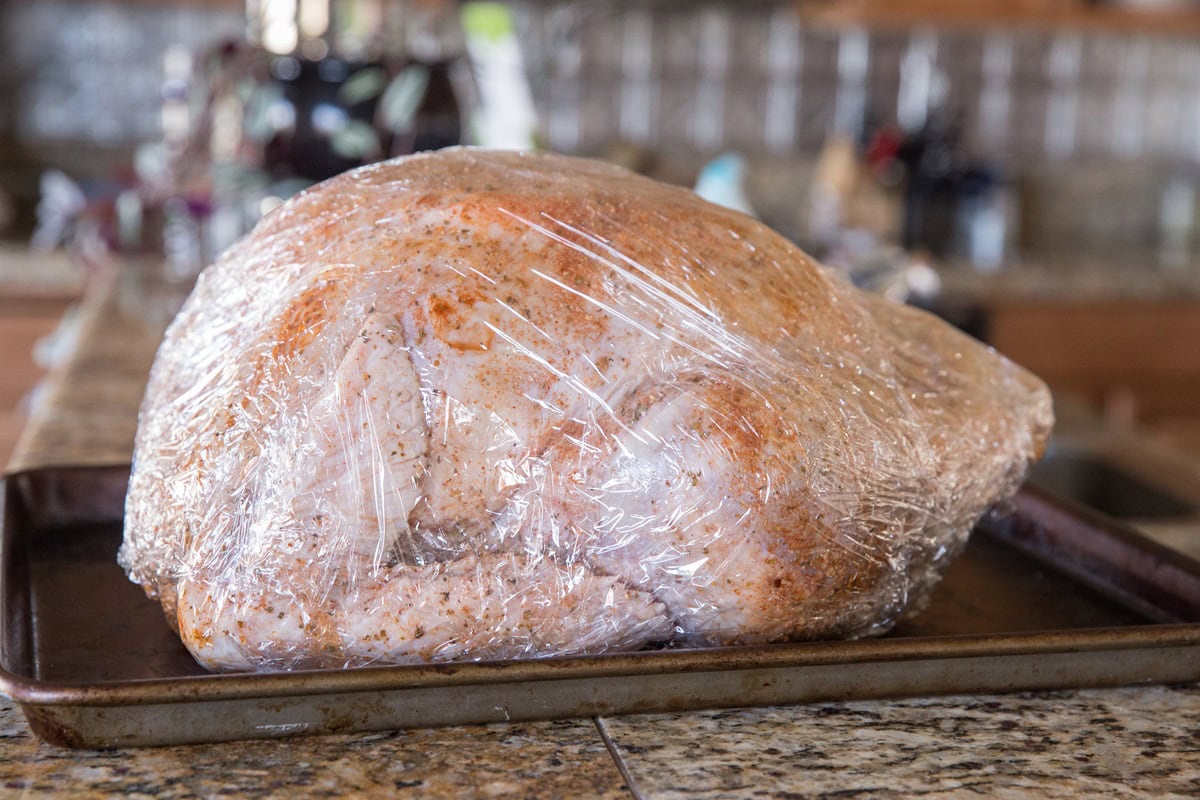 whole turkey covered in seasonings, wrapped in plastic wrap for dry brining.