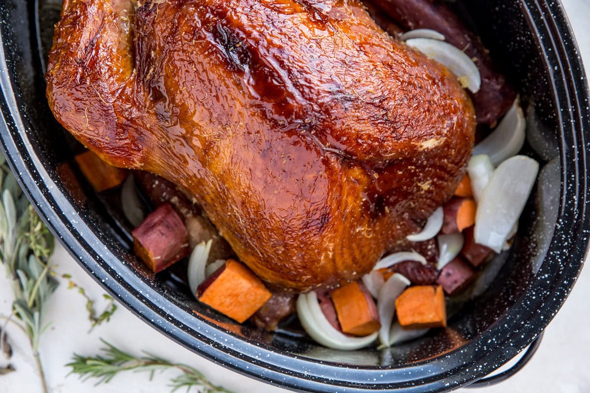 Dry brined turkey in a large roasting pan with sweet potatoes and onions at the bottom of the pan.